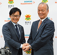 会見場で固い握手を交わす鈴木理事長（右）と森社長